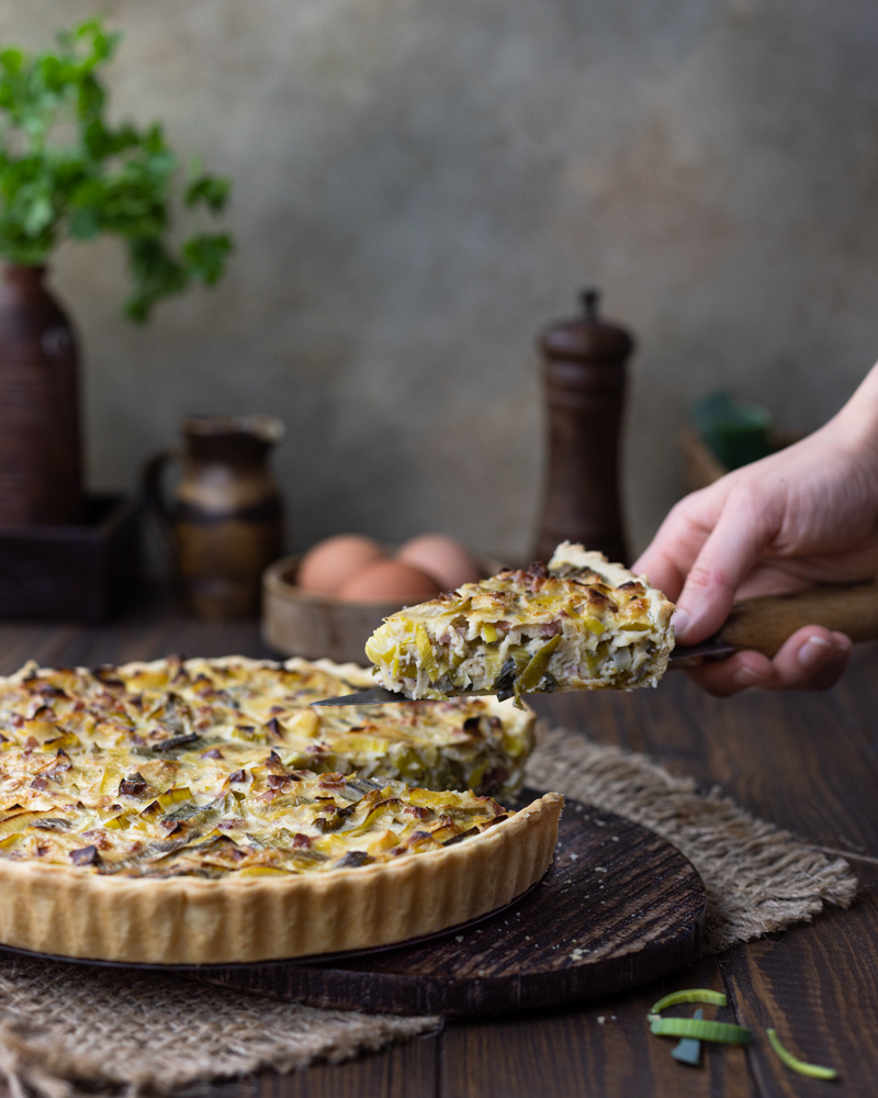 Ein Stück von der Lauch-Speck Quiche mit einer Kuchengabel entnehmen